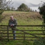 Jeremy Clarkson leans on a wooden gate looking out across a grassy field on his farm.