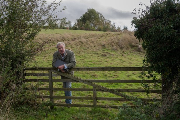Jeremy Clarkson leans on a wooden gate looking out across a grassy field on his farm.