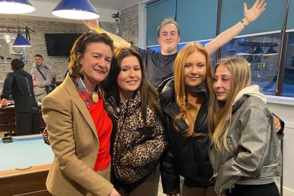 First Minister Eluned Morgan, a woman with short blonde hair, smiling and chatting with a group of people inside a social club bar.