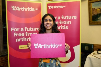 Olivia holding an Arthritis UK banner at a parliamentary event raising awareness of arthritis in young people.