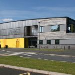 The modern exterior of Ysgol Maesydderwen comprehensive school in Ystradgynlais on a sunny day, showing the school's yellow and grey facade.