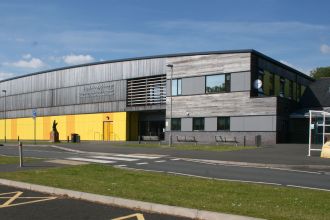 The modern exterior of Ysgol Maesydderwen comprehensive school in Ystradgynlais on a sunny day, showing the school's yellow and grey facade.