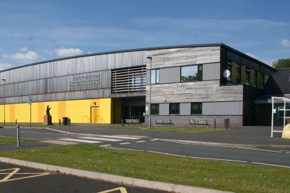 The modern exterior of Ysgol Maesydderwen comprehensive school in Ystradgynlais on a sunny day, showing the school's yellow and grey facade.