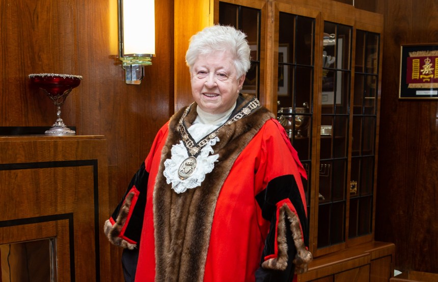 A smiling Penny Matthews wearing the official red and fur-trimmed robes and chain of office of the Deputy Lord Mayor of Swansea, standing in a wood-panelled room.
