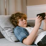 a boy using a smartphone while lying on a sofa