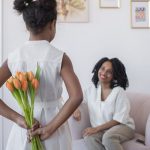 a girl surprising her mother with a bouquet of flowers