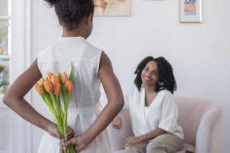 a girl surprising her mother with a bouquet of flowers