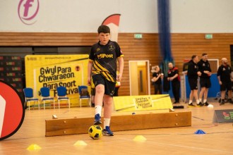 Boy dribbling a football through cones during an indoor para sport activity session in Swansea.