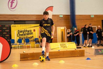 Boy dribbling a football through cones during an indoor para sport activity session in Swansea.