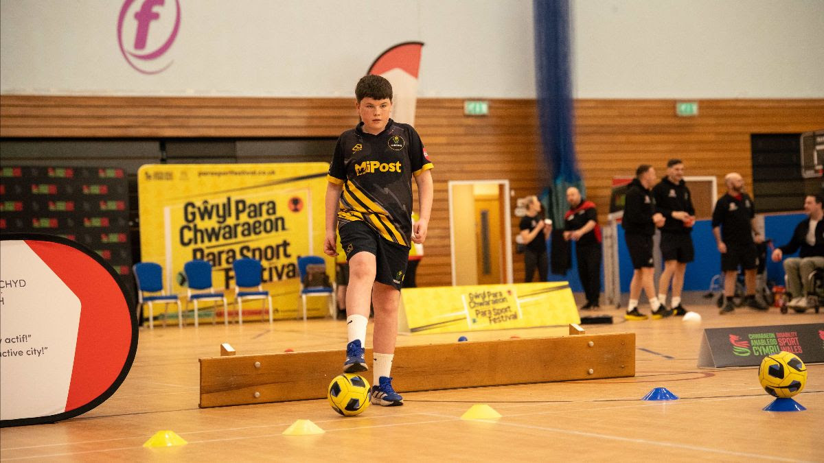 Boy dribbling a football through cones during an indoor para sport activity session in Swansea.