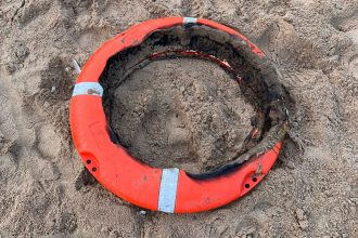A badly burned orange lifebuoy ring lying partially buried in sand on Aberavon Beach, its foam interior destroyed by fire
