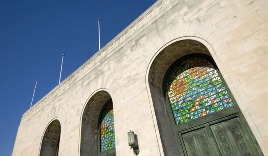 The exterior of Swansea's Guildhall showing the arched Portland stone facade, ornate decorative details and colourful stained glass windows against a blue sky