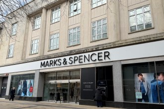 The exterior of the Marks and Spencer store on Oxford Street in Swansea city centre, showing the large branded fascia above the ground floor shopfront with display windows and a customer using the ATM outside