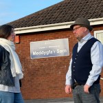 Carl Peters-Bond and Clare Treharne stand outside Meddygfa'r Sarn GP surgery in Pontyates, with the surgery's bilingual welcome sign visible on the wall behind them