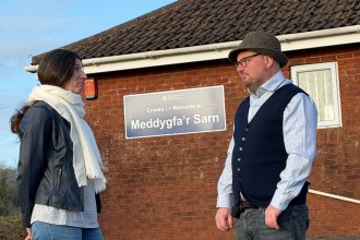 Carl Peters-Bond and Clare Treharne stand outside Meddygfa'r Sarn GP surgery in Pontyates, with the surgery's bilingual welcome sign visible on the wall behind them