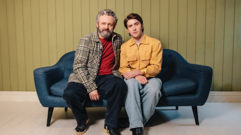 Michael Sheen and Callum Scott Howells seated together on a blue sofa