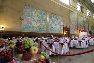 he main hall at Brangwyn Hall in Swansea set for a wedding reception, with the famous Frank Brangwyn panels lining the walls and tables dressed in white and red