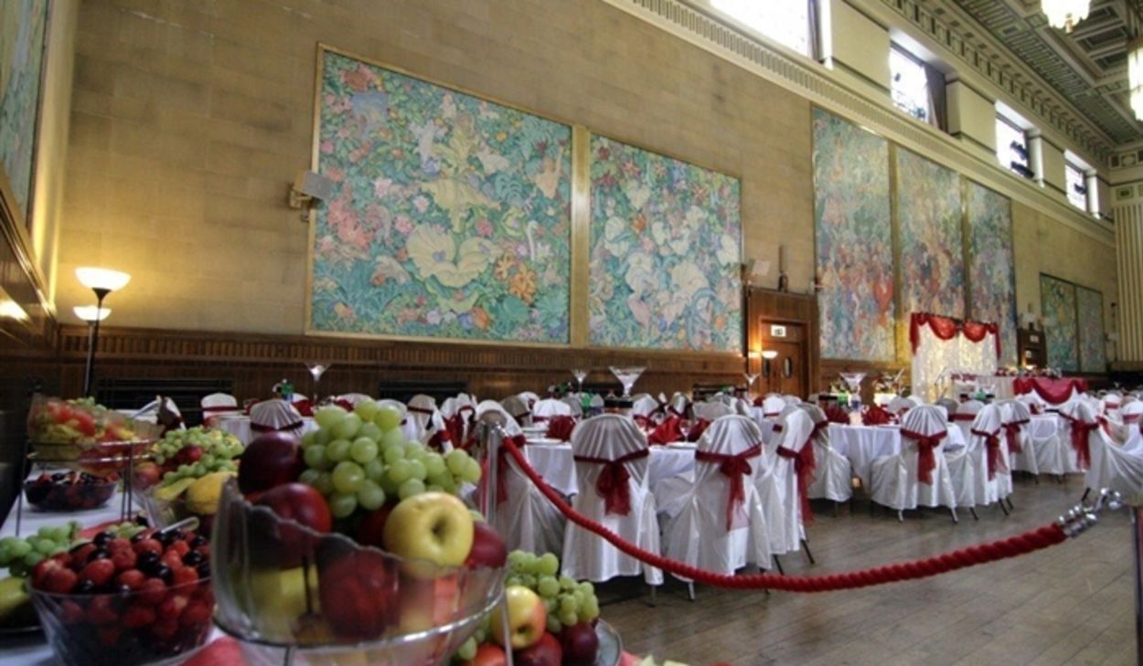he main hall at Brangwyn Hall in Swansea set for a wedding reception, with the famous Frank Brangwyn panels lining the walls and tables dressed in white and red