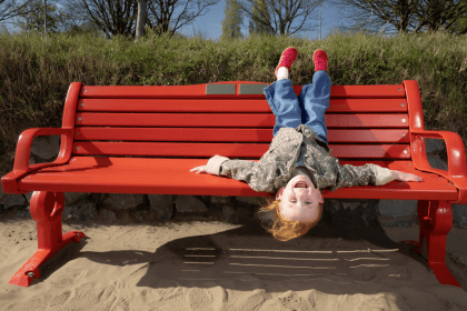 Five-year-old Esme Mariani laughing upside down on a red British Heart Foundation bench on Swansea Beach.