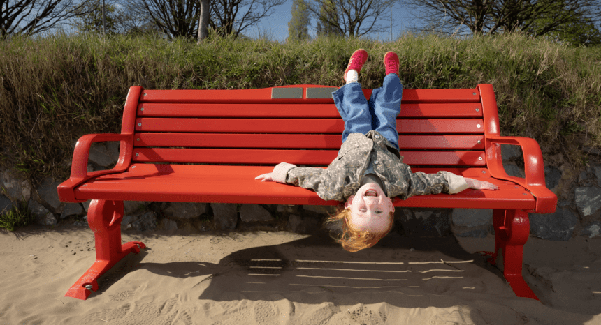 Five-year-old Esme Mariani laughing upside down on a red British Heart Foundation bench on Swansea Beach.