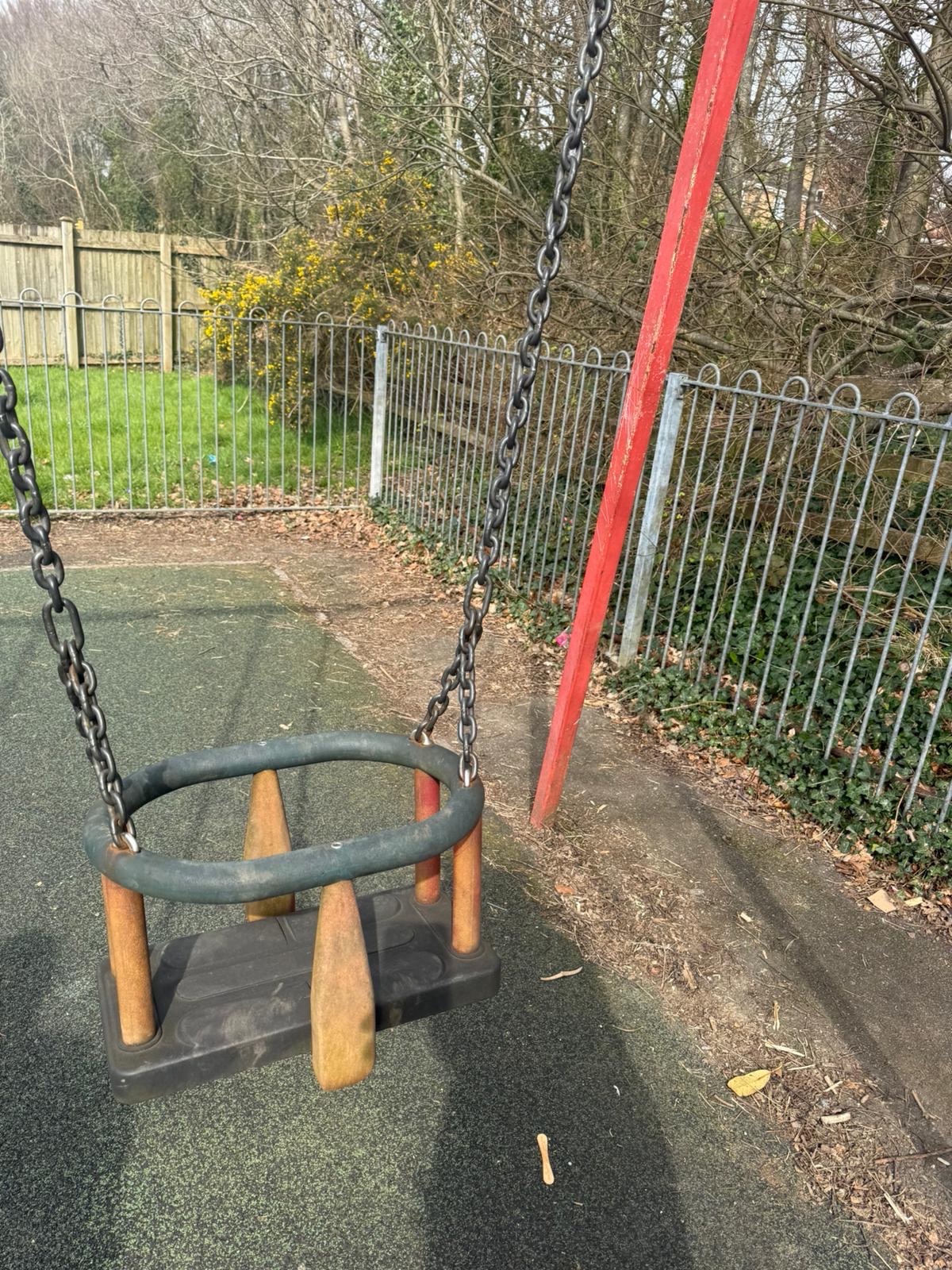Baby swing with rusting red frame at Coed Hirwaun children’s play park Port Talbot