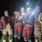 Five firefighters from Kidwelly Fire Station holding rescued lambs at night after culvert rescue.