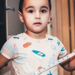 young child playing indoors with measuring tape