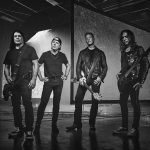 Black and white photo of Metallica's four members standing on a stage holding their instruments.