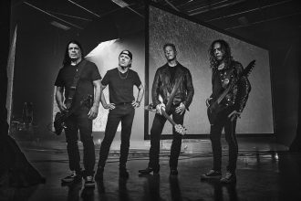 Black and white photo of Metallica's four members standing on a stage holding their instruments.