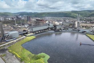 An aerial CGI visualisation of Tata Steel's Port Talbot plant, showing the planned new Electric Arc Furnace facility integrated with the existing steelworks, with the site's industrial buildings, cooling towers and surrounding hills of the Afan Valley in the background