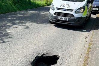 Sinkhole in the middle of a residential road with a South Wales Police van parked behind it on Cecil Road, Gowerton.