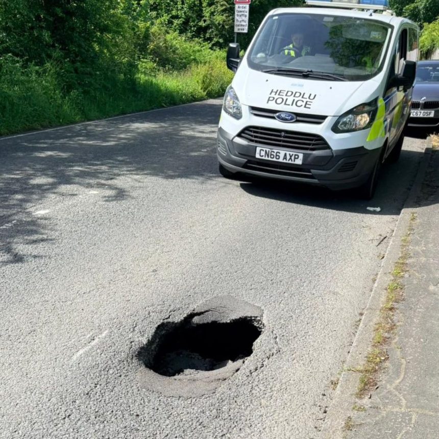 Sinkhole in the middle of a residential road with a South Wales Police van parked behind it on Cecil Road, Gowerton.