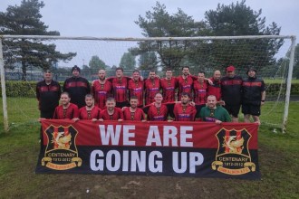 Cwm Albion FC players celebrate under the goalposts holding a banner reading 'We are going up' after securing promotion to Division One of the Swansea Senior League