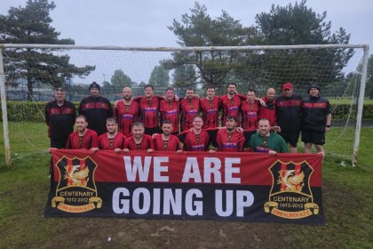 Cwm Albion FC players celebrate under the goalposts holding a banner reading 'We are going up' after securing promotion to Division One of the Swansea Senior League