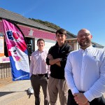 Tom Mogridge, Toby Link-Jones and James Smale-Davies stand together on a sunny seafront promenade outside the pink-painted GG's Gelato kiosk, with a branded GG's Gelato flag and menu board visible behind them