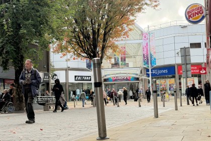 A view of the TGJones store at the entrance to the Quadrant Shopping Centre in Swansea, with the chain's blue signage visible to the right of the centre's main entrance, alongside a Post Office sign, Burger King logo and shoppers walking in the autumn pedestrianised area
