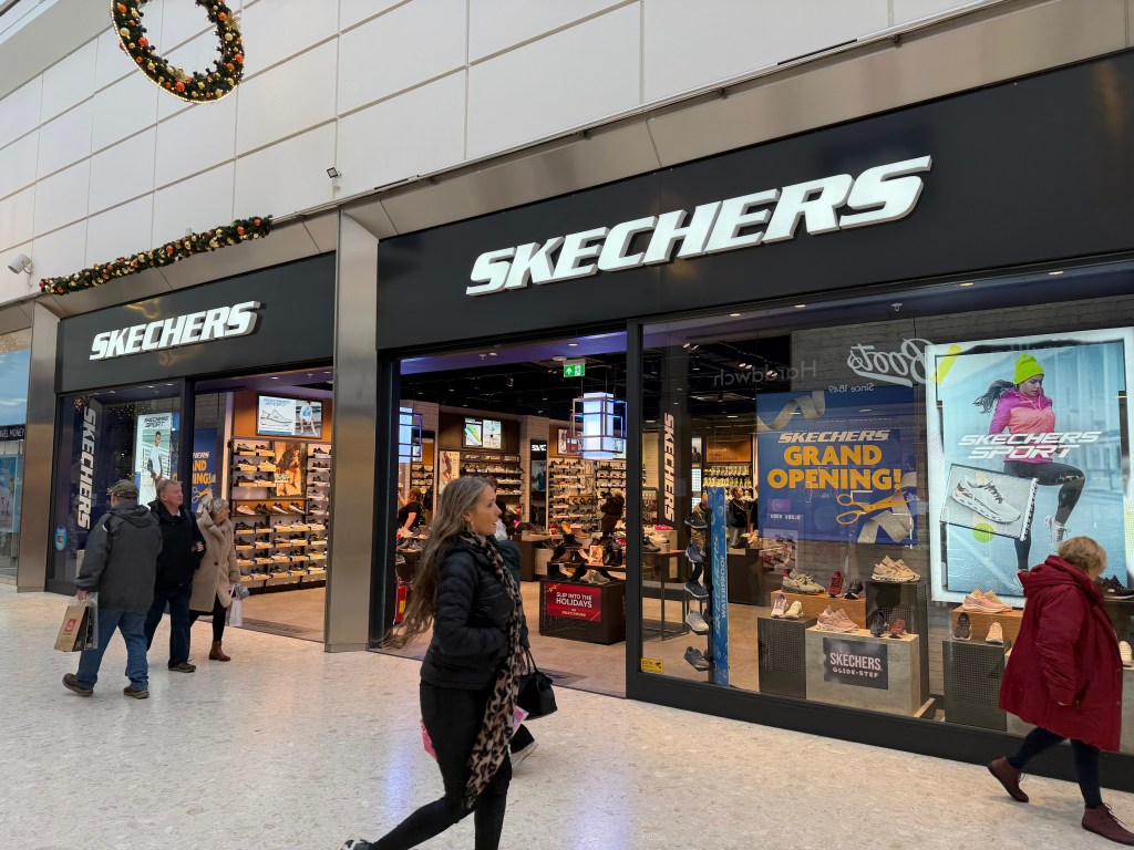 The Skechers store front inside the Quadrant Shopping Centre, with a 'Skechers Grand Opening' display and a 'Skechers Sport' advert in the window, and shoppers walking past the entrance.