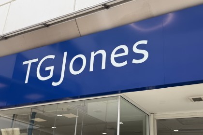 Close-up of a large blue TGJones shop fascia above a glass shopfront, photographed from below at an angle.