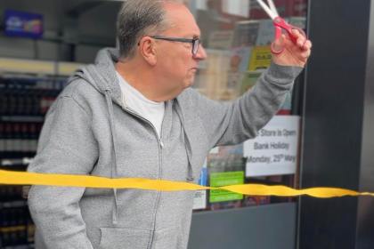Kev Johns MBE raises a pair of scissors to cut a yellow ribbon at the entrance to the new CK Foodstores in Bynea.
