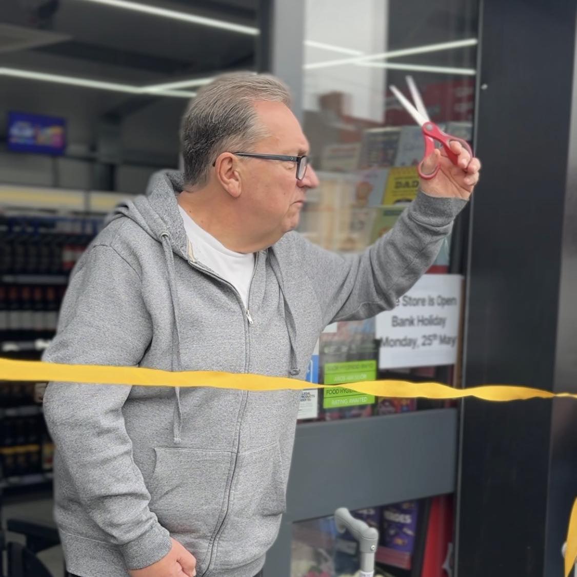 Kev Johns MBE raises a pair of scissors to cut a yellow ribbon at the entrance to the new CK Foodstores in Bynea.