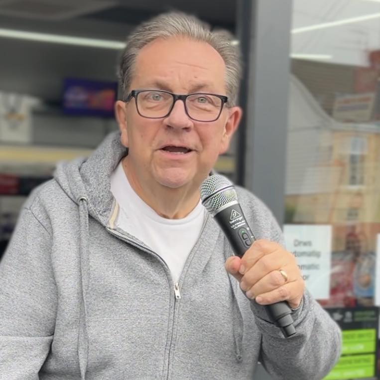 Kev Johns MBE speaking into a handheld microphone outside the new CK Foodstores in Bynea.