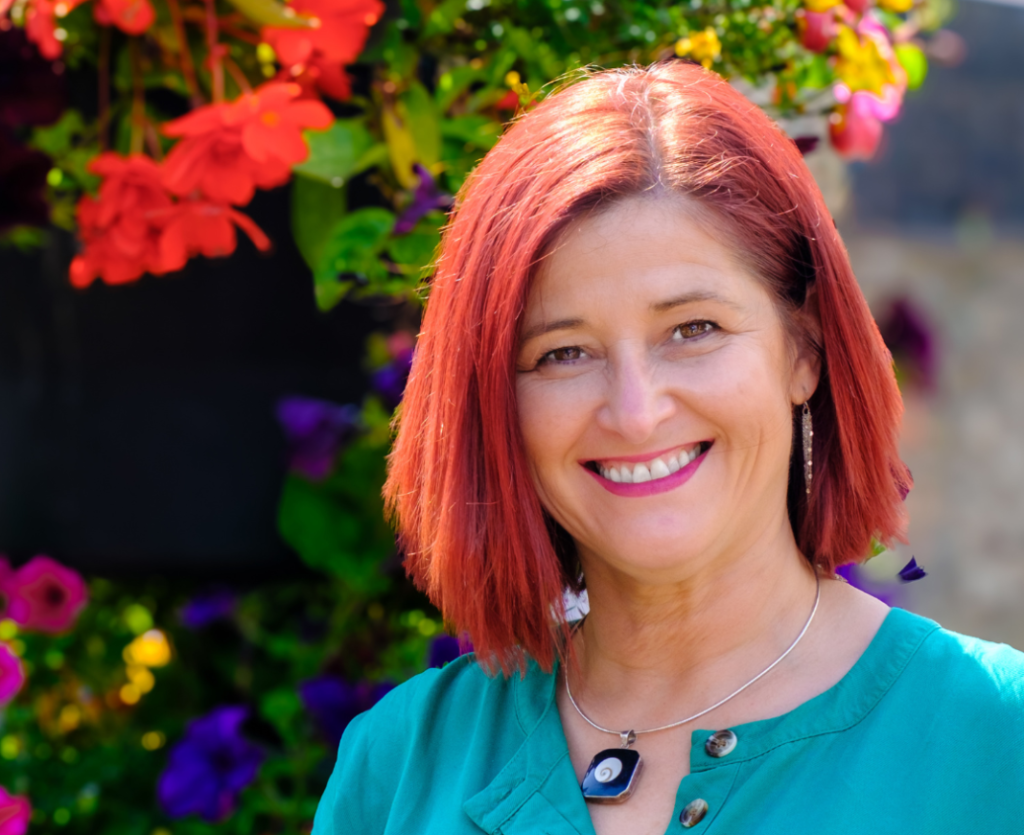 Plaid Cymru Senedd candidate Mari Arthur smiles in front of colourful hanging flower baskets