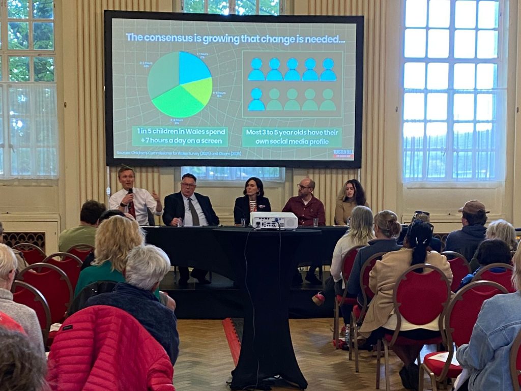 A projected presentation slide reading "The consensus is growing that change is needed", showing statistics that one in five children in Wales spend more than seven hours a day on a screen and that most three to five year olds have their own social media profile, with the expert panel visible below.