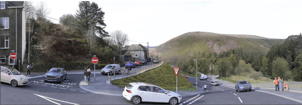 An artist's impression of the new Maesteg Road junction in Cymmer looking north-west, showing a new central grassed island separating traffic flows, no-entry signs on a closed road to the left, and families on a new pavement to the right with the Afan Valley visible beyond.