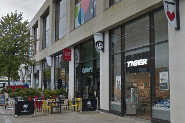 Exterior of the Flying Tiger store in Swansea on Princess Way, with the brand's red heart and toy soldier logo on a sign jutting out from the building. Coffee#1 and Zinco Lounge sit alongside, with outdoor seating in the foreground.