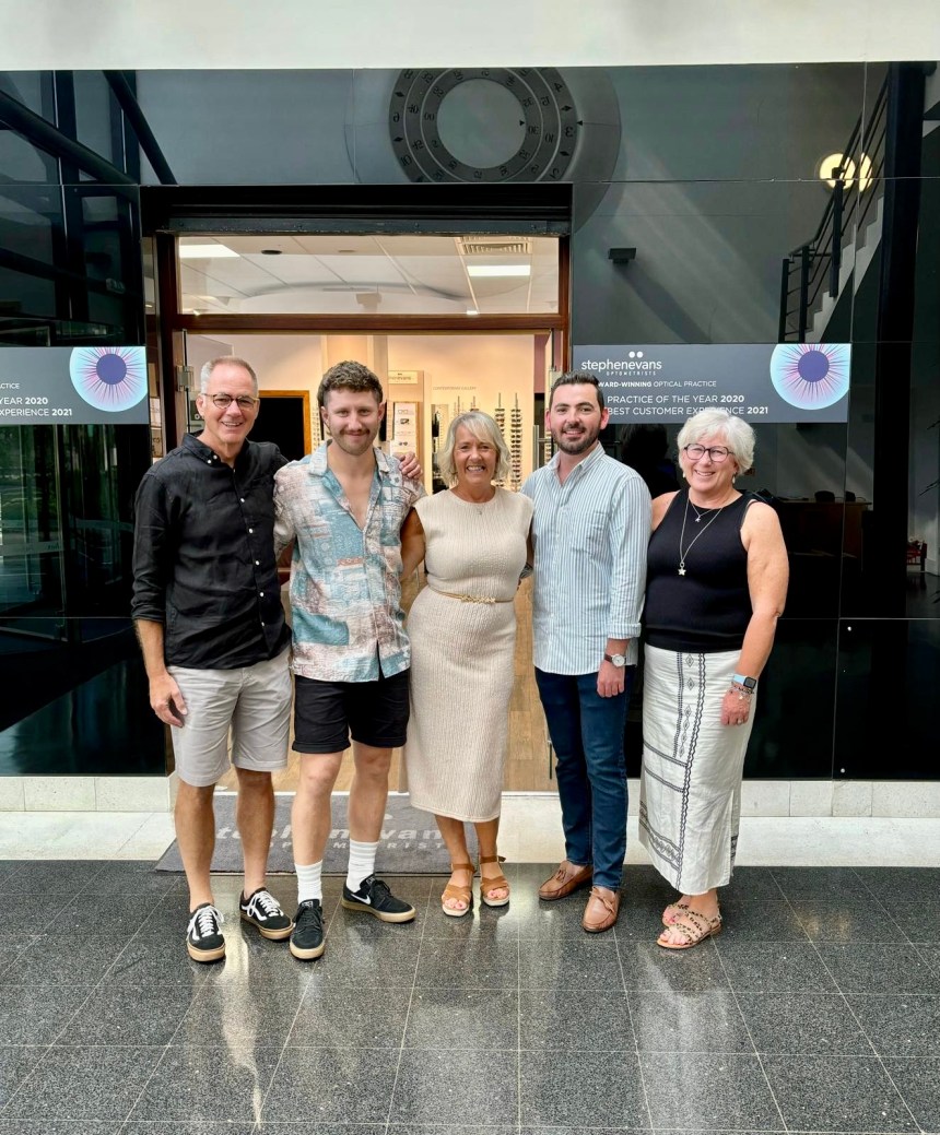 Five members of the Stephen Evans Optometrists team smiling outside their Kings Road practice in Swansea's SA1 Waterfront (left to right): Stephen Evans, Henry Evans, Caroline Paul, Ben Packer and Chrissy Evans, with the practice's award-winning signage visible in the background.