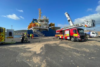 The bow of the JSP Samsø, a blue-hulled multi-purpose cargo ship registered in Madeira, moored at King's Dock in Swansea on a clear blue sky day