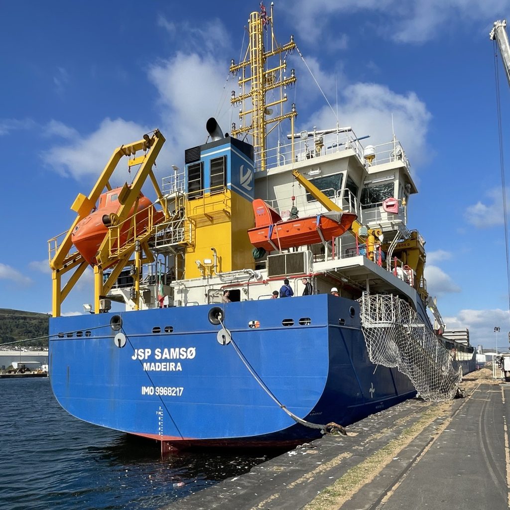 A Mid and West Wales Fire and Rescue Service turntable ladder appliance and Welsh Ambulance Service vehicle alongside the JSP Samsø cargo ship at King's Dock in Swansea, with firefighters and paramedics on the dockside