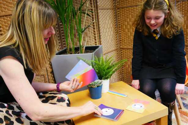 A young woman in school uniform sits in conversation with a smiling adult counsellor, both engaged in a one-to-one wellbeing session as part of The Exchange programme