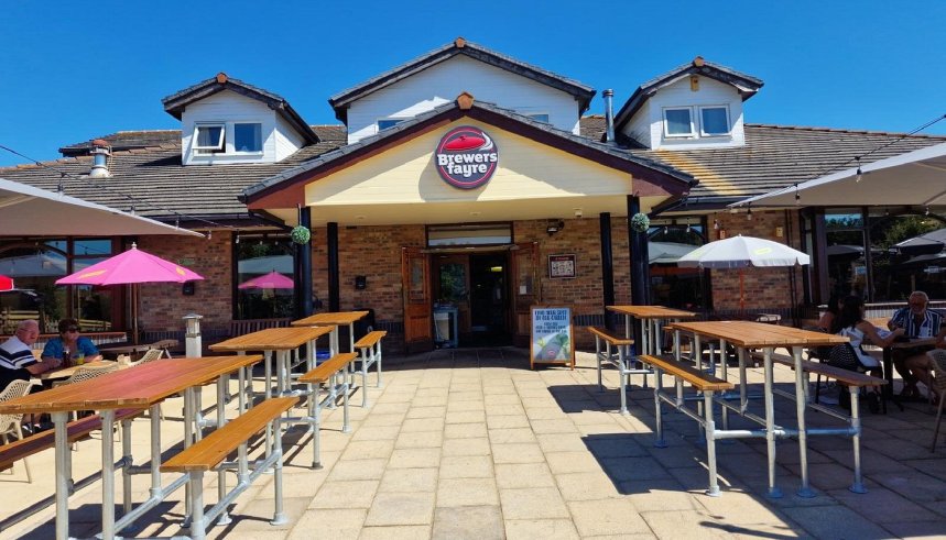 The exterior of The Sandpiper Brewers Fayre pub restaurant on Sandy Road in Llanelli, showing the Brewers Fayre branded frontage with an outdoor beer garden with wooden picnic tables and parasols on a sunny day